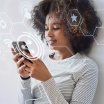 Mulher encostada na parede segurando um celular com ícones flutuando, representando uma estratégia Omnichannel