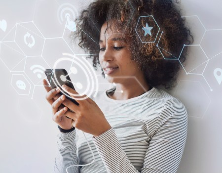 Mulher encostada na parede segurando um celular com ícones flutuando, representando uma estratégia Omnichannel