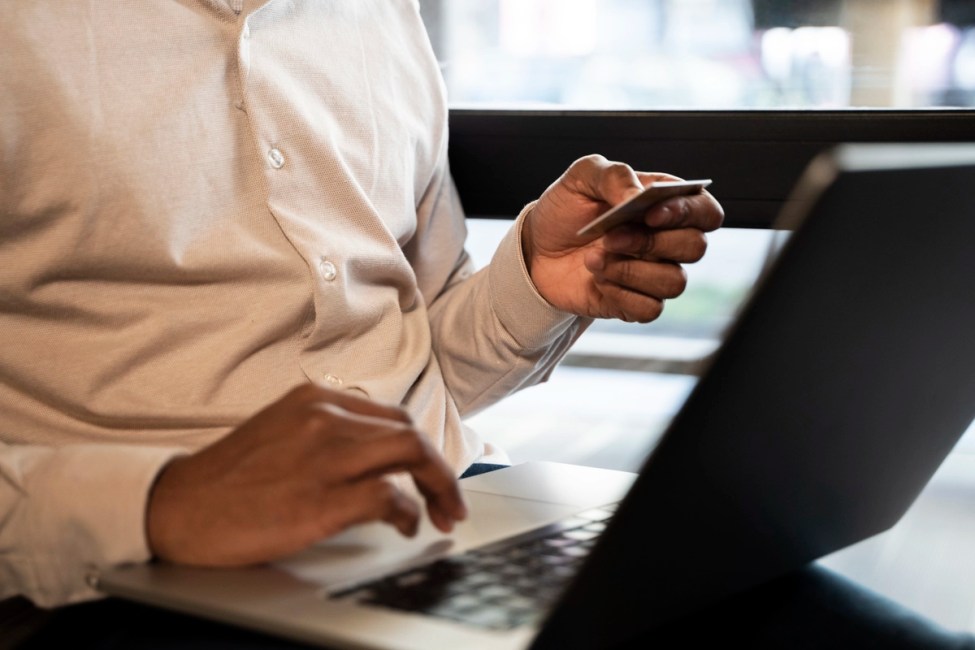 Homem sentado em frente a um notebook segurando um cartão de crédito usando o programa de cashback para empresas