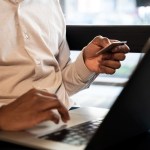 Homem sentado em frente a um notebook segurando um cartão de crédito usando o programa de cashback para empresas