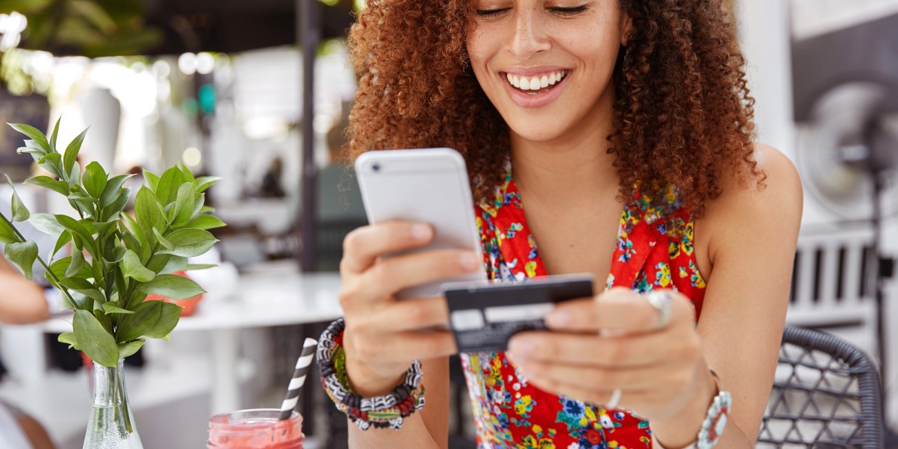 Mulher olhando para o celular e o cartão para aprender como usar cashback